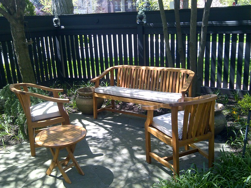 Teak bench and chairs with gently curved backs and white cushions and a small round folding table