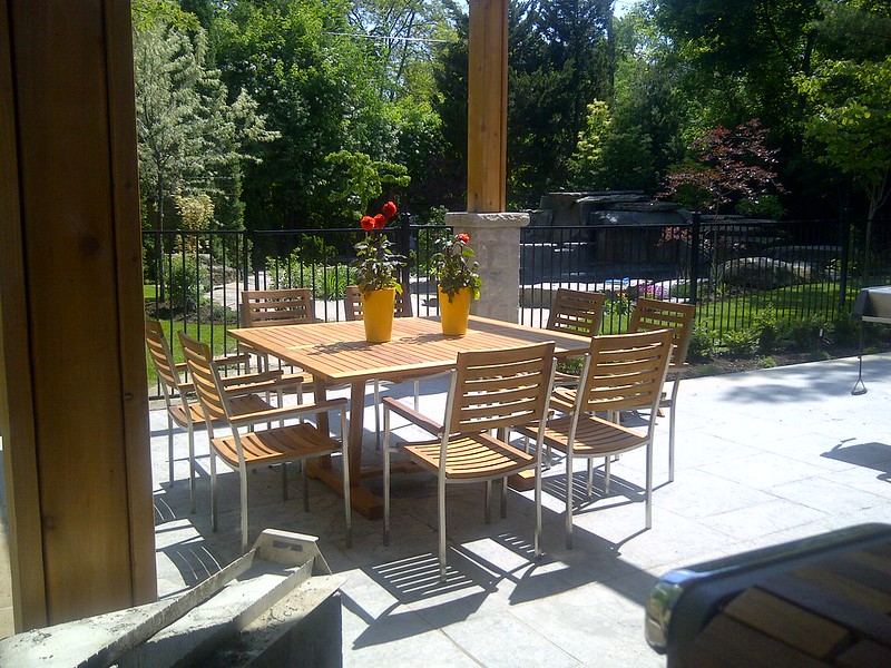 Square teak dining table surrounded by chairs with metal frames and teak slats