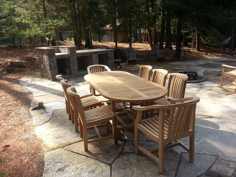 Light teak oval dining table surrounded by armless and arm chairs with gently curved backs